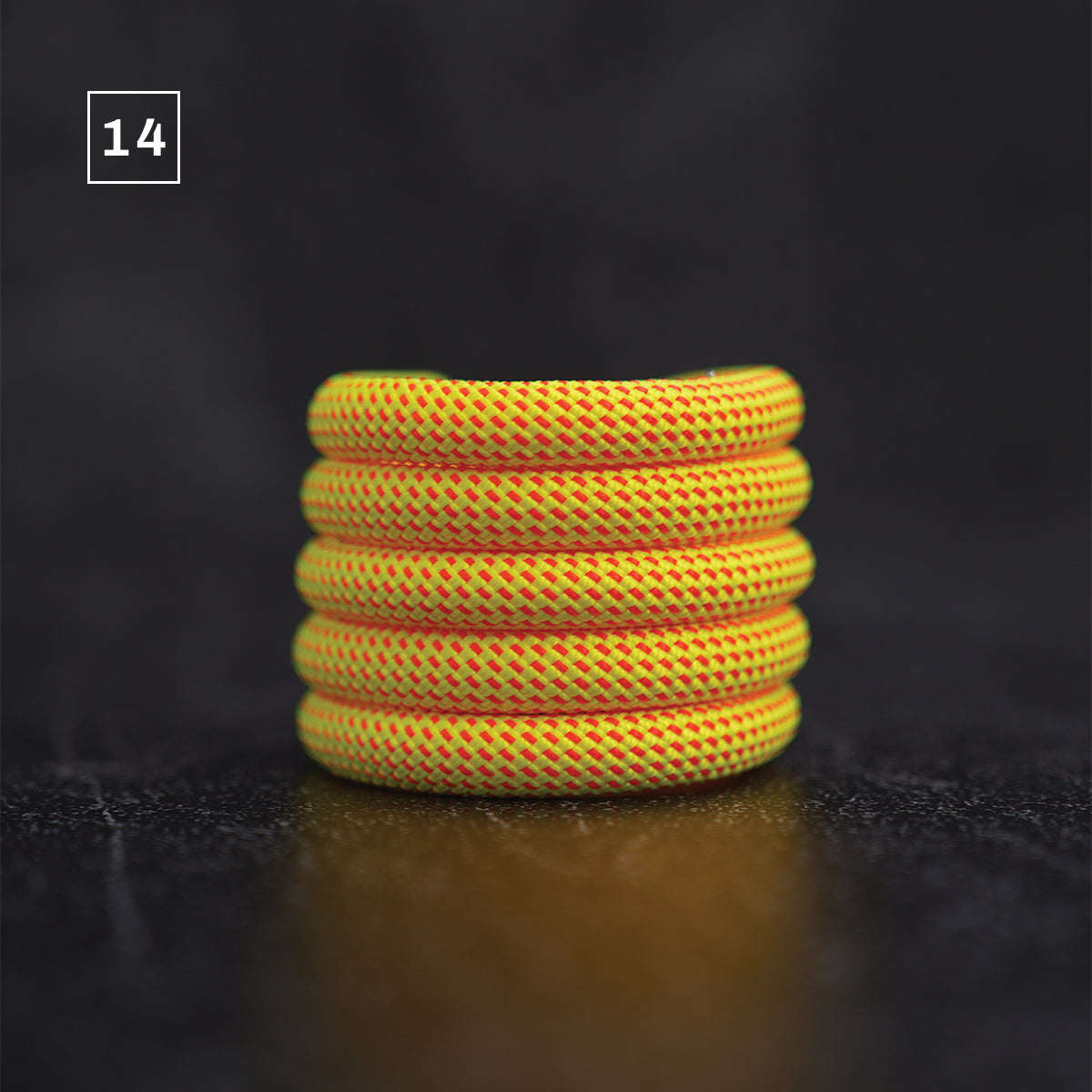 A stack of five yellow and orange braided rope rings, likely leather or paracord, displayed on a dark reflective surface with a black background. A small white square containing the number '14' is in the top-left corner.