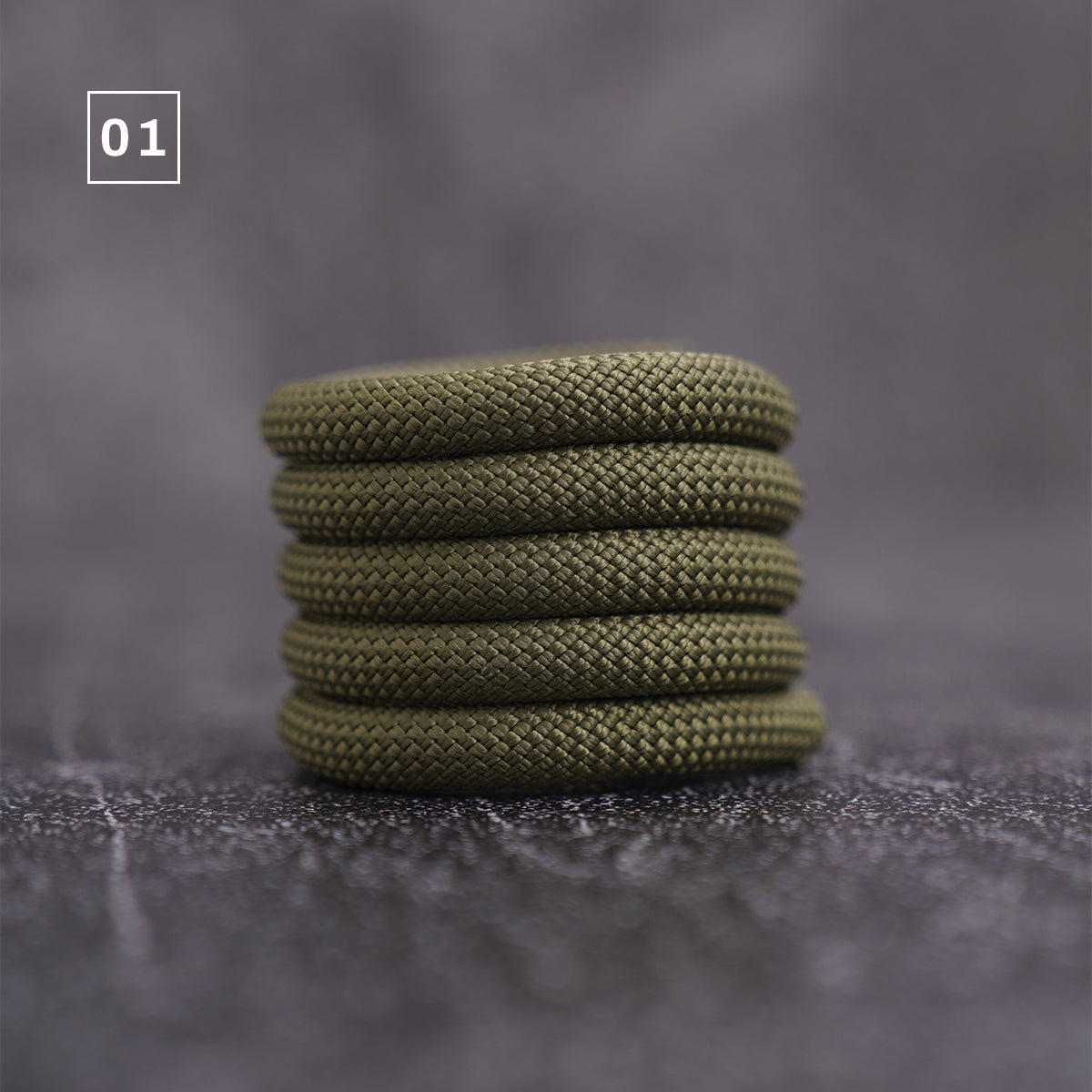 A stack of five olive green braided cord loops, shown on a textured gray surface with a '01' label overlay in the top left corner.