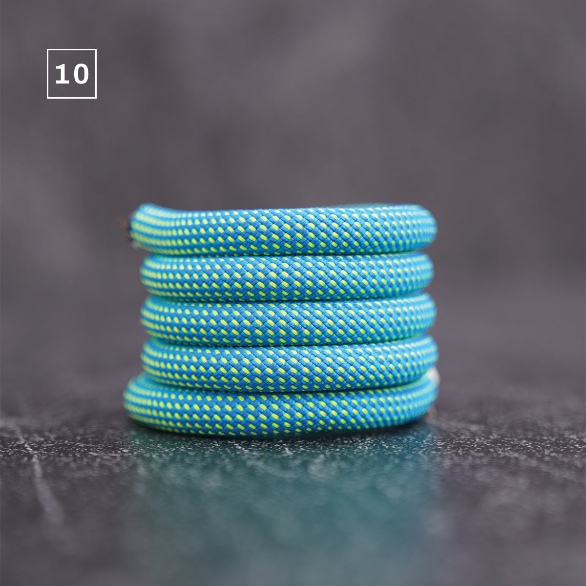 A stack of five turquoise blue braided rope rings with yellow accents, resting on a dark textured surface with a gray background. A small white square containing the number '10' is in the top-left corner.