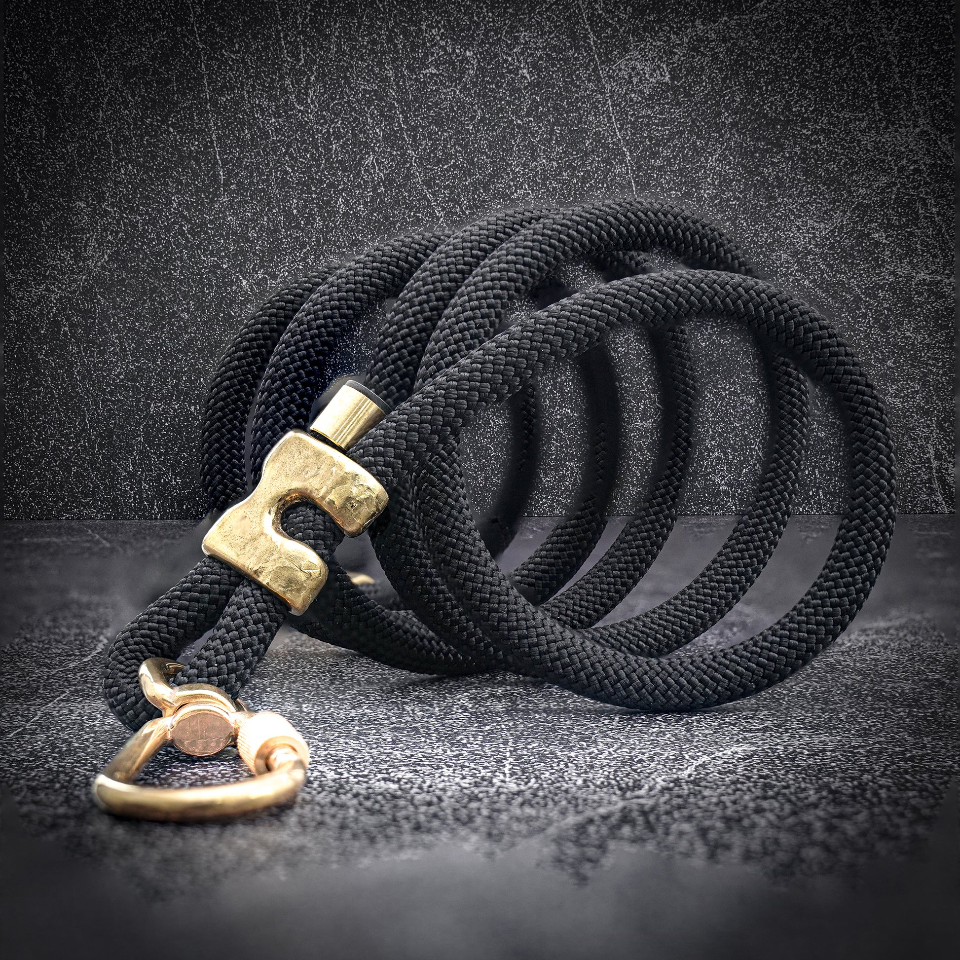 black rope dog leash with brass coiled with a gray background