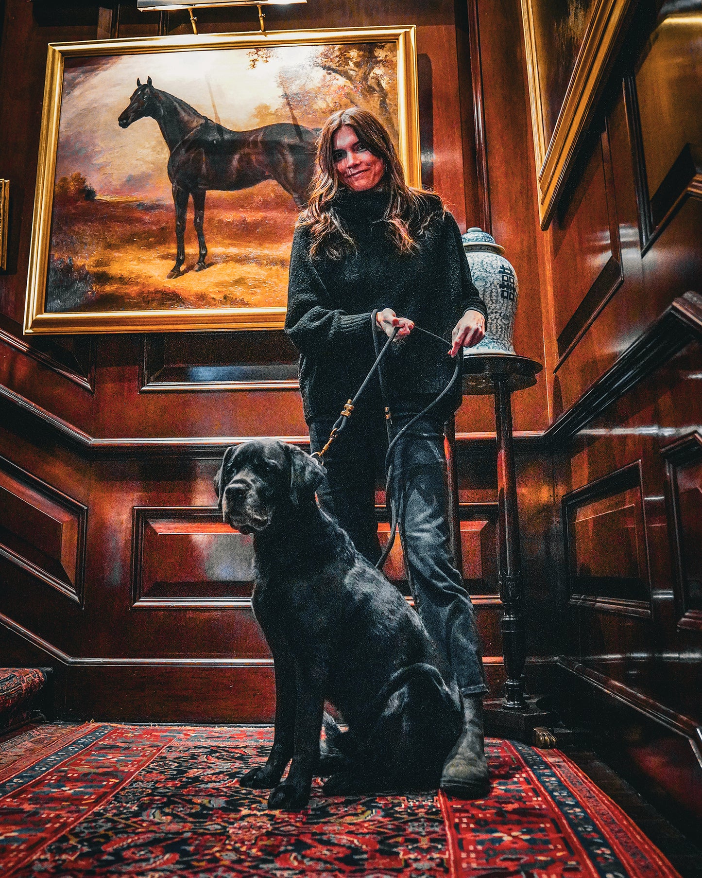 Woman with a dog in a room with wooden walls and a horse painting.