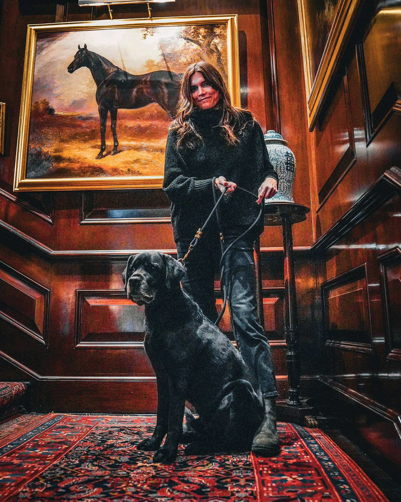 Woman with a dog in a room with wooden walls and a horse painting.