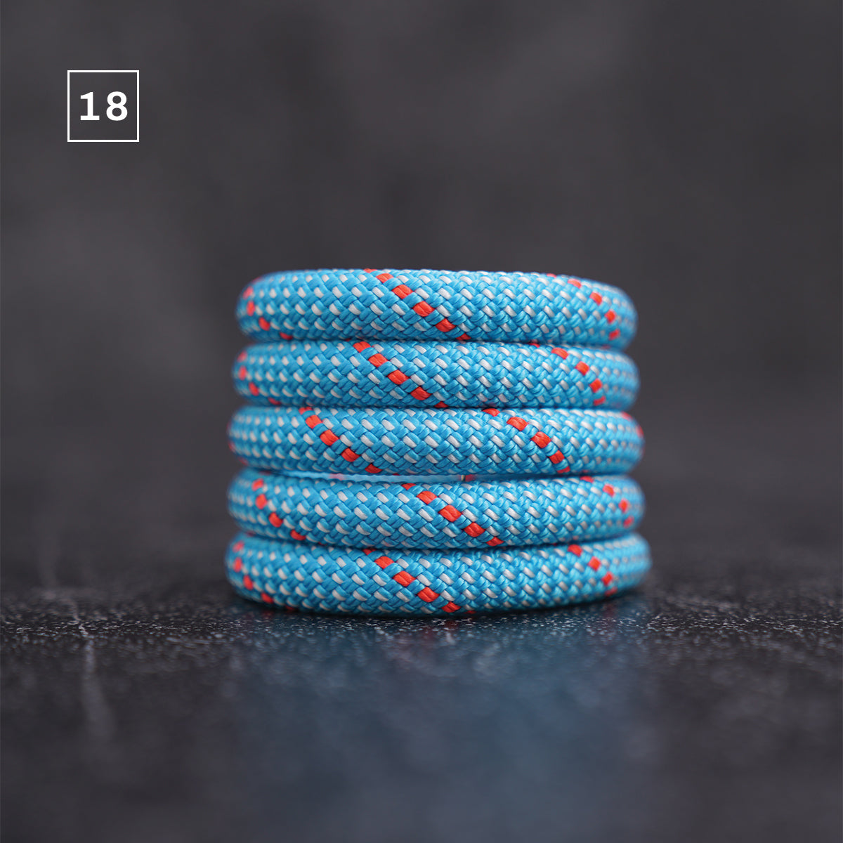 A stack of five blue braided rope rings with red and white woven details, set against a dark gray background. A small white square containing the number '18' is in the top-left corner.