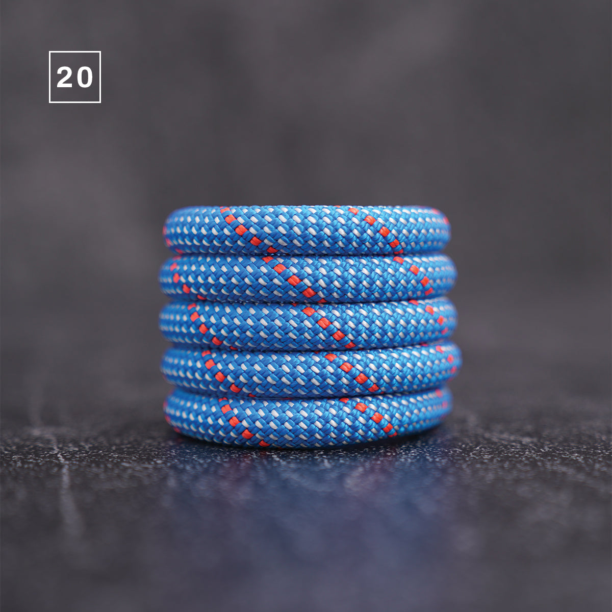 A stack of 20 blue braided cord or rope rings with red and white woven details, displayed on a dark textured surface.