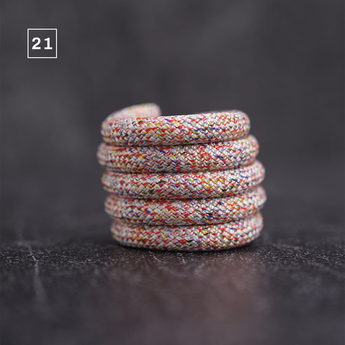 A braided rope with a multicolor flecked pattern of red, blue, yellow, and white threads, coiled on a dark textured surface. A small white square with the number '21' is in the top-left corner.