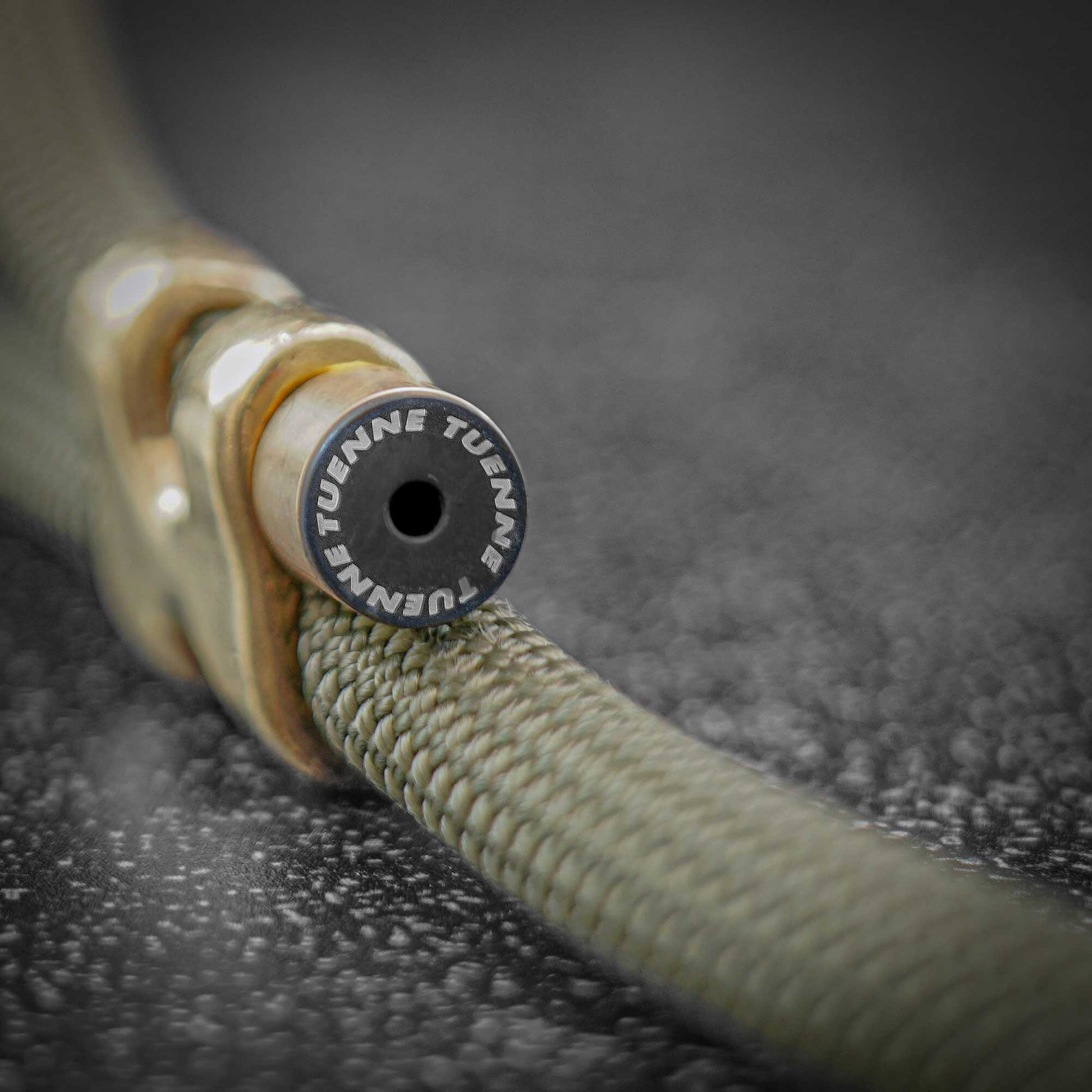 Close-up of a braided hose connector with a circular black end cap printed with the brand name TUENNE TUENNE.