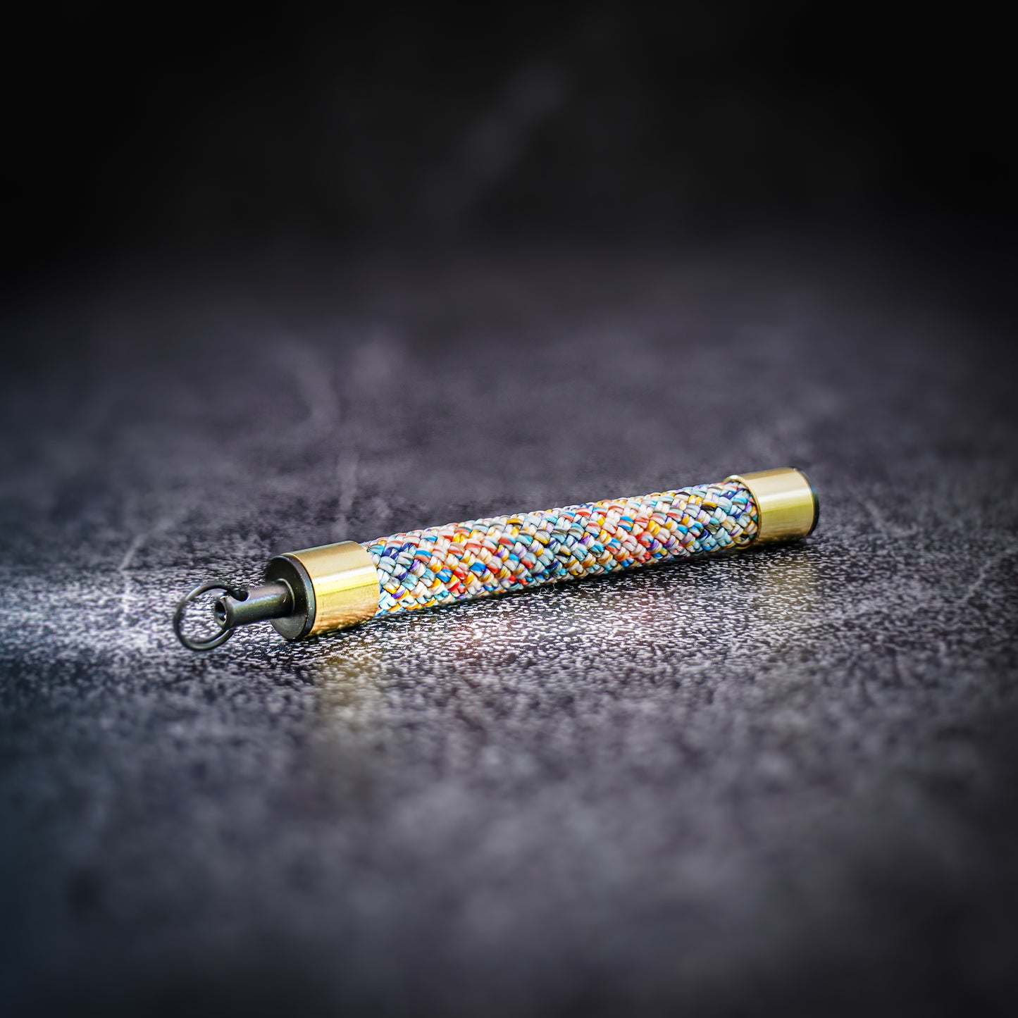 Multi color rope Keychain featuring brass sleeves and a Tuenne logo-engraved endcap, resting on a textured surface.