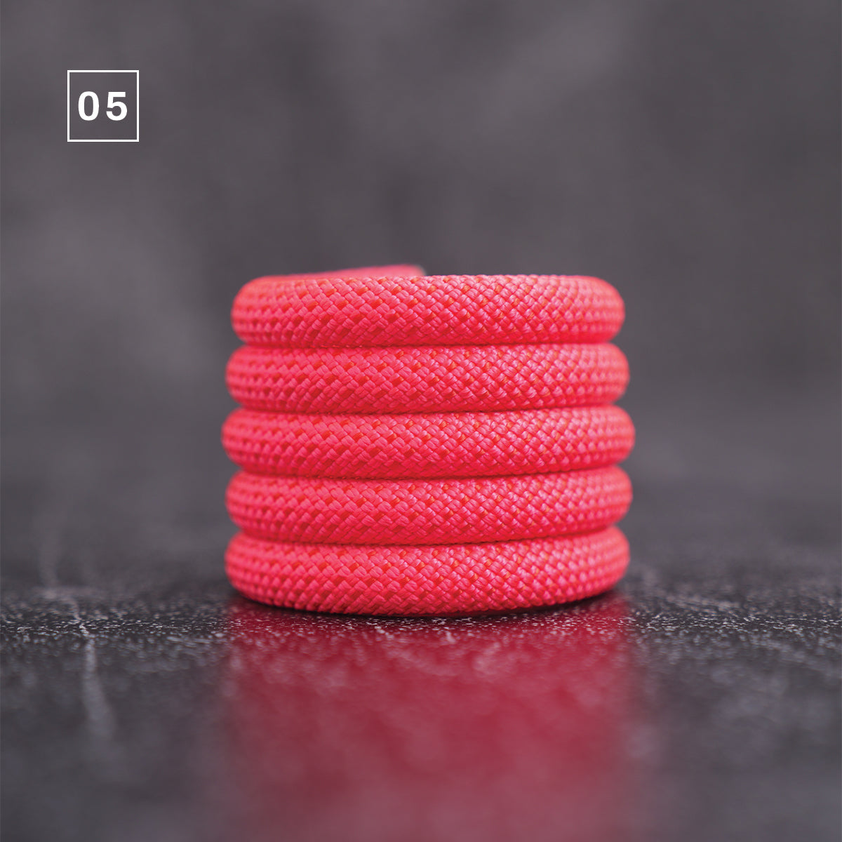 A bright red braided cord or rope coil standing upright on a dark reflective surface, with a small white square label in the upper left containing the number 05.