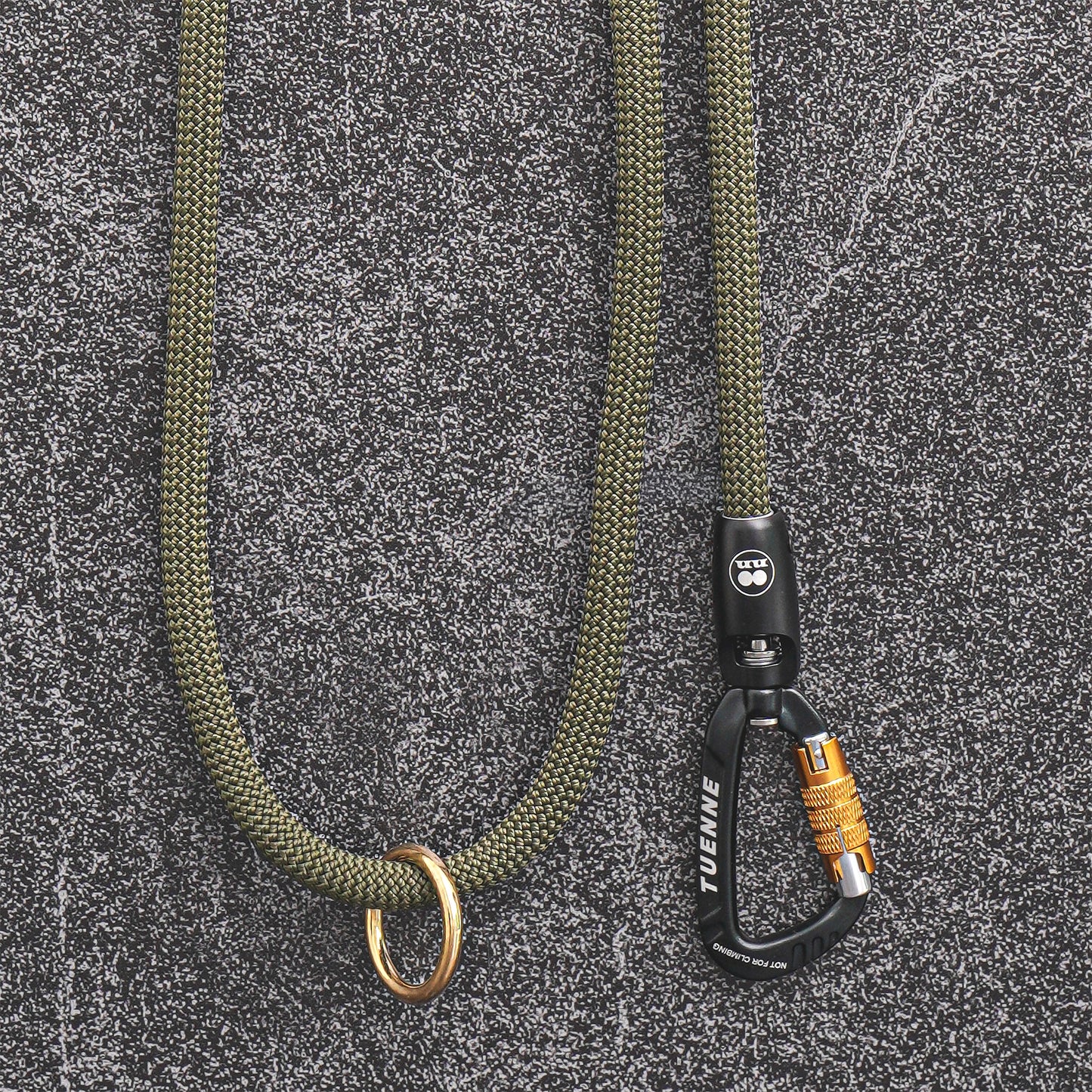 An olive green paracord lanyard with a brass ring and a black carabiner featuring a yellow lock, displayed on a textured gray background.