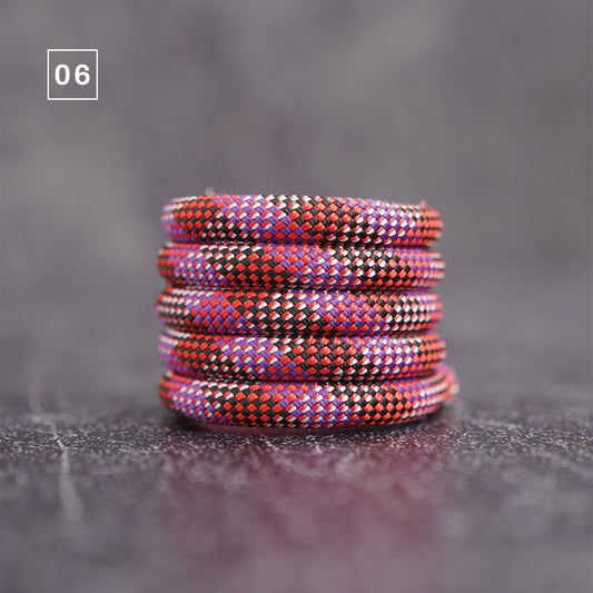 A stack of five braided elastic bands or cords in a red, purple, and black pattern, displayed on a dark textured surface with a gray background. A small white square containing the number '06' is in the top-left corner.