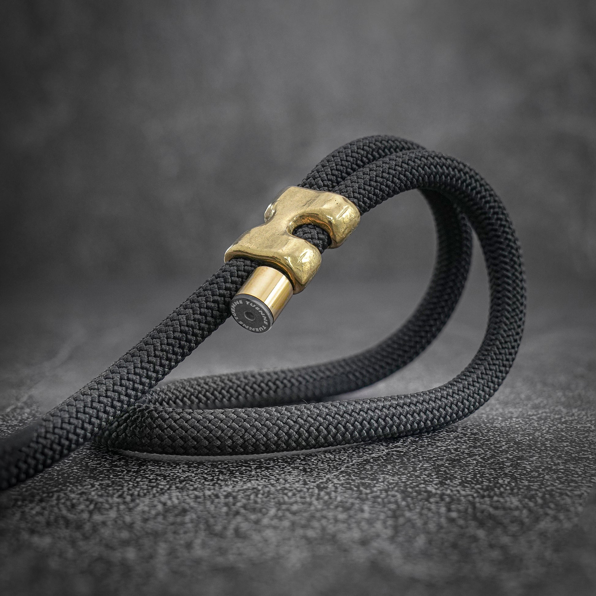 Black rope with a brass clasp on a dark gray background