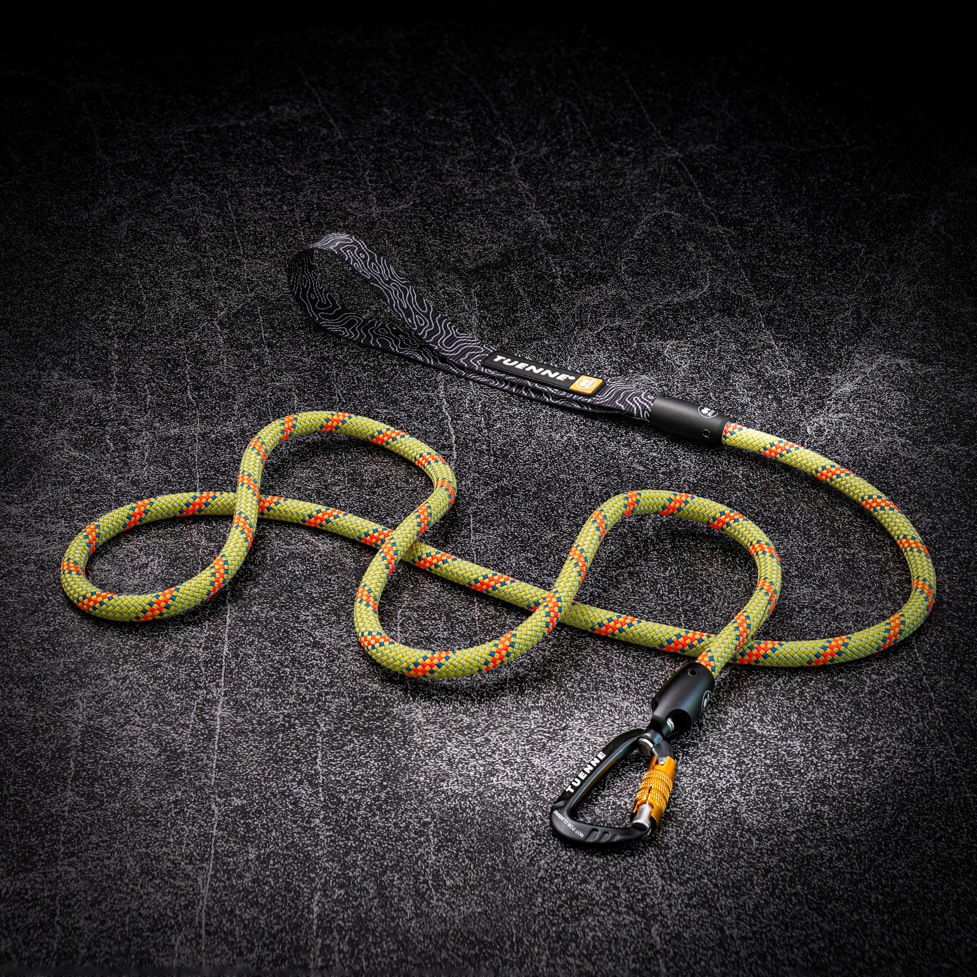 A green and orange climbing rope with a black loop handle and black carabiner, displayed on a dark textured background.