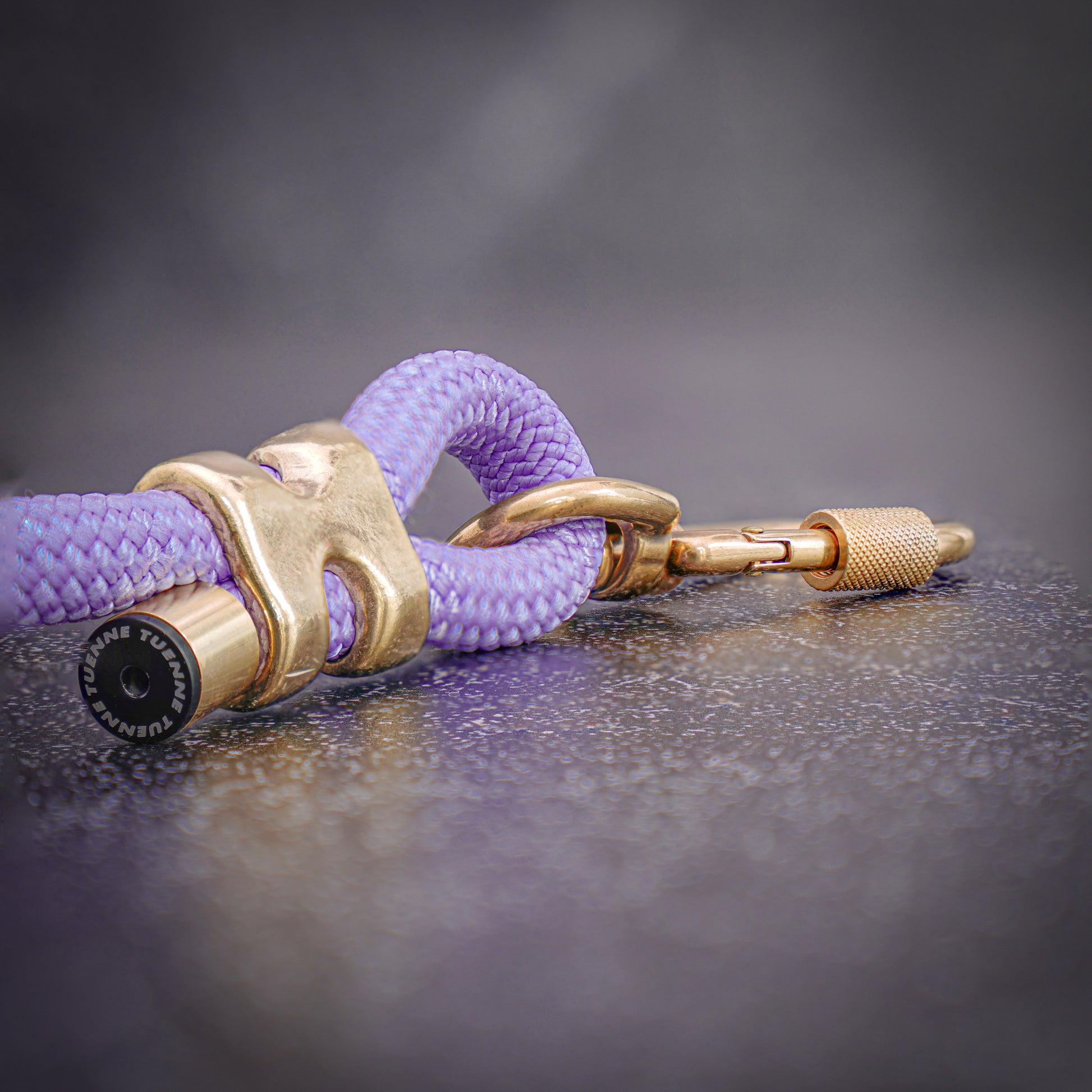 closeup of lavender rope leash with a brass carabiner and brass crimp on a slate surface