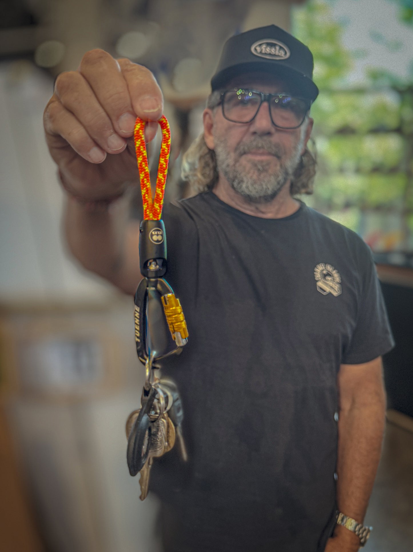 Man holding a keychain with a carabiner and keys, wearing a black cap and t-shirt.