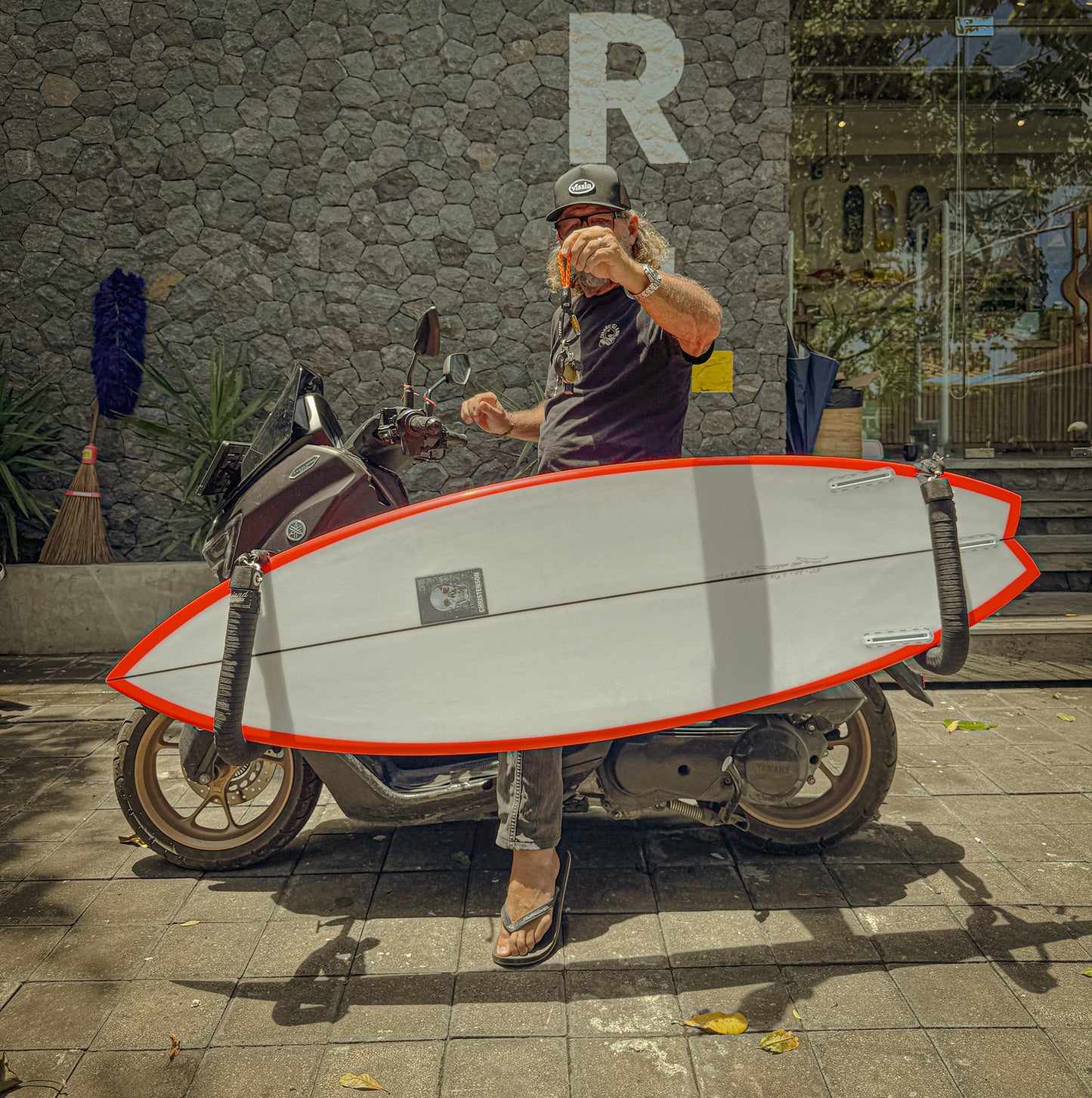 Man holding a orange-rope-keychain on a scooter with a surfboard on it. 