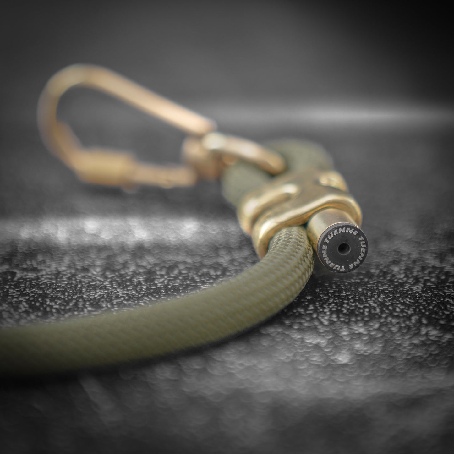 Close-up of a green rope dog leash with a brass carabiner on a dark textured surface