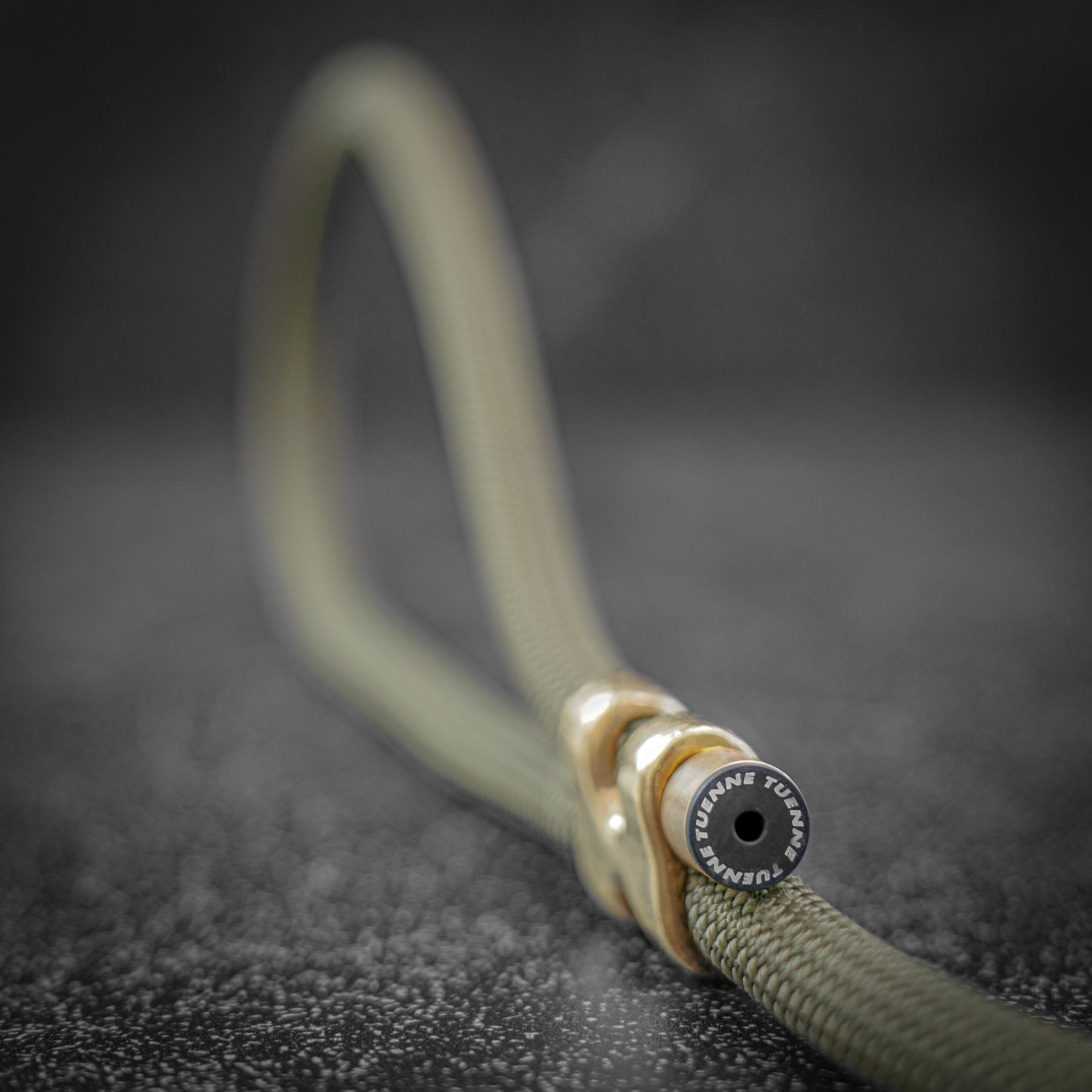 Close-up of a olive rope dog leash with a brass crimp on a dark textured background