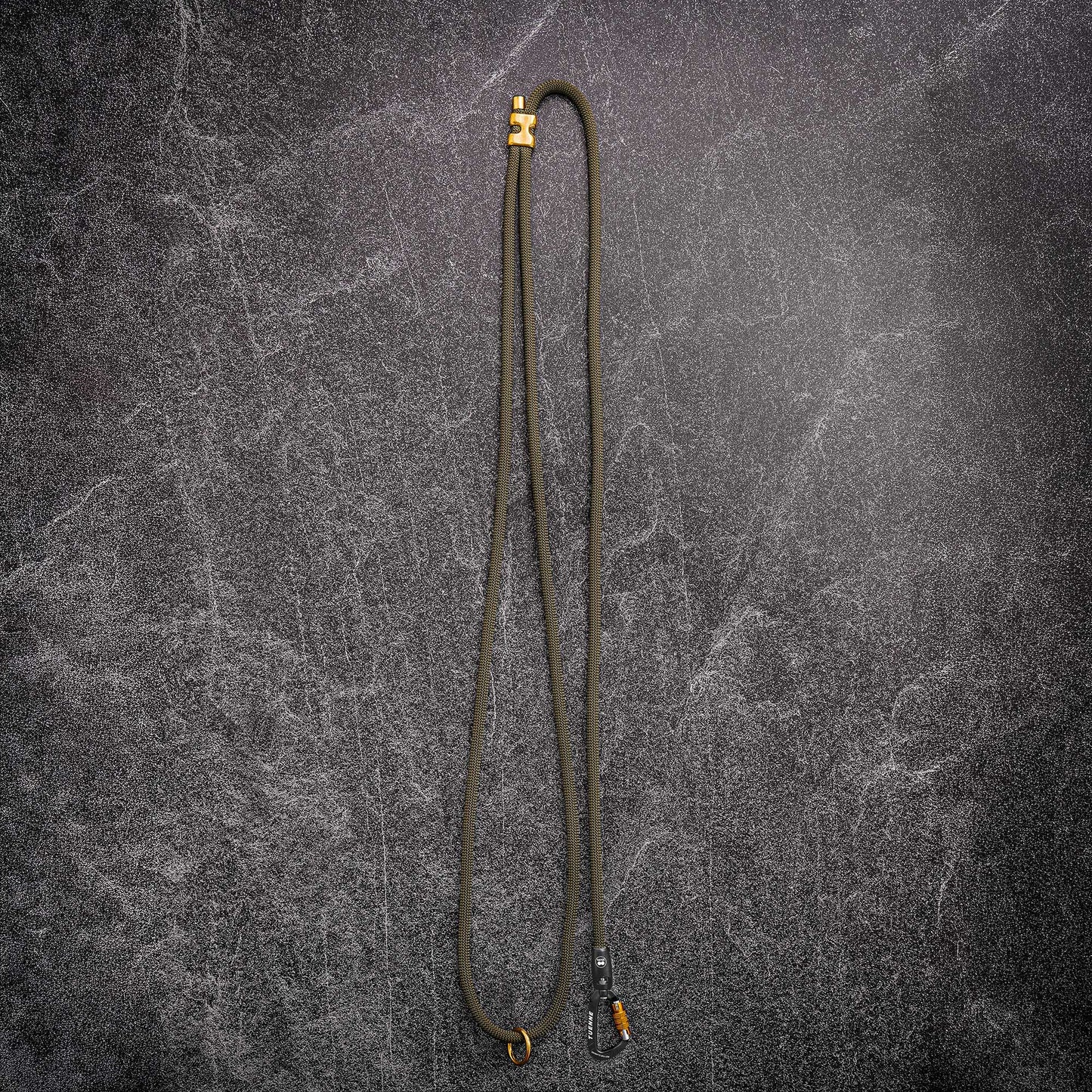 A long olive green rope handsfree leash or with brassl hardware at both ends, laid flat on a dark textured gray background.