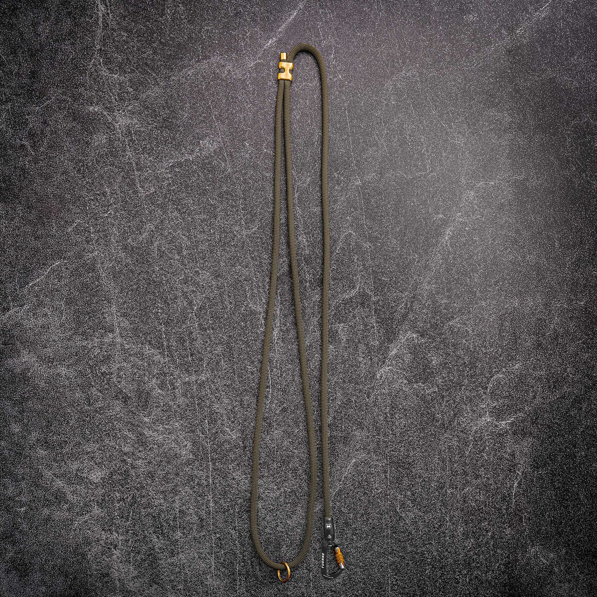 A long olive green rope handsfree leash or with brassl hardware at both ends, laid flat on a dark textured gray background.