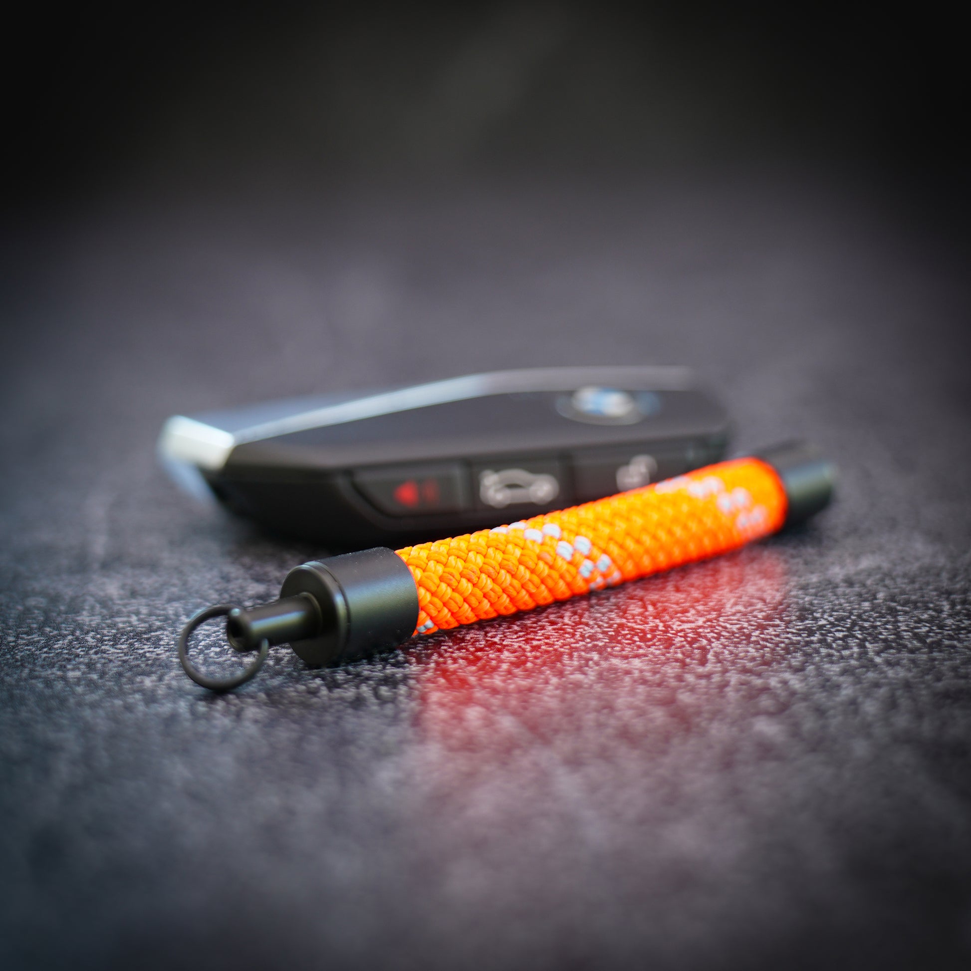 Orange rope keychain on a dark textured surface next to a bmw car key