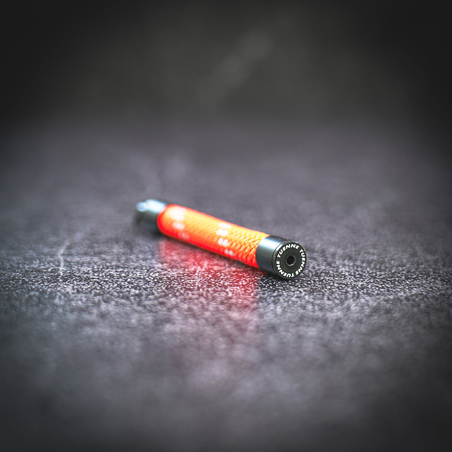 Orange rope keychain on a dark textured surface with an endcap engraved with a tuenne logo